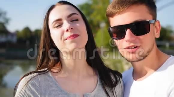 一对年轻幸福的夫妇看着镜头的肖像在池塘附近的绿色夏季公园里的浪漫情侣快乐视频的预览图