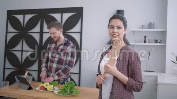 幸福的妻子在厨房的画像满意的女人看丈夫谁准备健康的饮食从蔬菜为视频的预览图