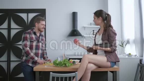 有魅力的胡须雄性从新鲜蔬菜和蔬菜中准备美味的健康沙拉雌性则坐在桌子上视频的预览图