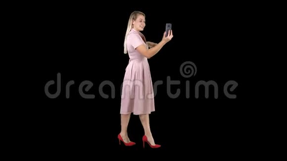 穿粉色衣服的年轻女子走路时用智能手机录制视频博客视频的预览图