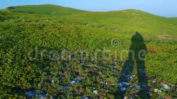 一个旅行者在一片山地草地和蓝天背景上的影子视频的预览图