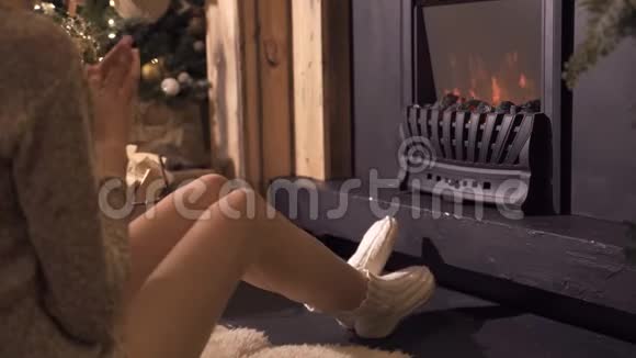 在圣诞树的背景下坐在壁炉旁的年轻漂亮女孩视频的预览图