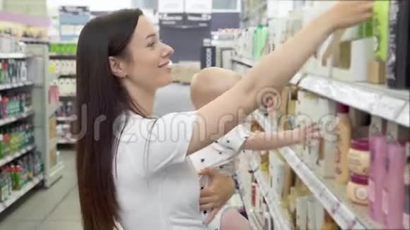 漂亮的女人带着小儿子在超市购物年轻的妈妈在市场上为家人选择洗发水视频的预览图