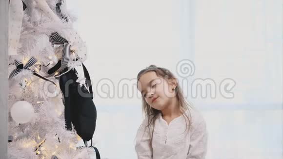 小女孩对装饰精美的圣诞树完全着迷圣诞树上有灯球和袜子视频的预览图