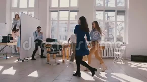 两位年轻有趣的女性办公室同事与多民族公司员工一起跳舞庆祝成功慢动作视频的预览图