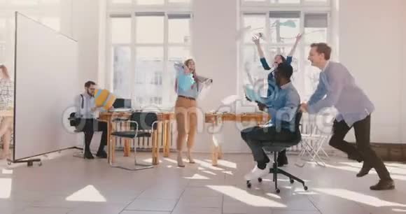 慢动作有趣的年轻疯狂非裔美国商人骑着办公椅与多民族团队庆祝胜利视频的预览图