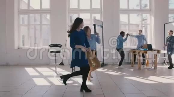 两个年轻有趣的女性商业伙伴一起跳舞庆祝胜利与多民族公司员工慢动作视频的预览图