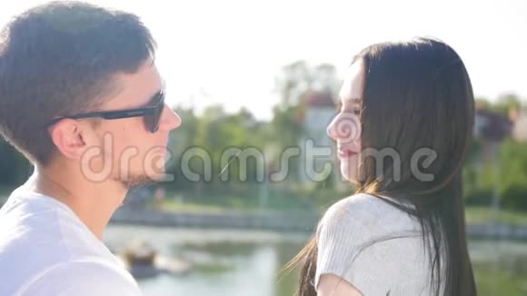 在池塘附近的绿色夏季公园里的浪漫情侣他们彼此亲近交谈一起快乐太阳视频的预览图