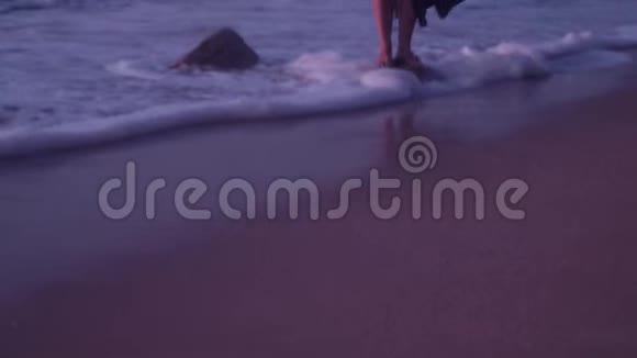 穿着黑色衣服的女人站在海浪中的石头上泡沫夏天晚上视频的预览图