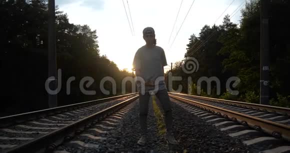 4k年轻有魅力的黑发男子在日落时分在铁路轨道上跳舞慢动作视频的预览图