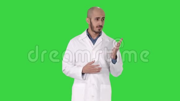 中年医生穿着医疗制服用手掌指着绿色的摄像机视频的预览图