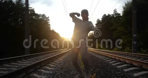 4K一个有魅力的家伙在日落时分在铁路轨道上跳舞视频的预览图