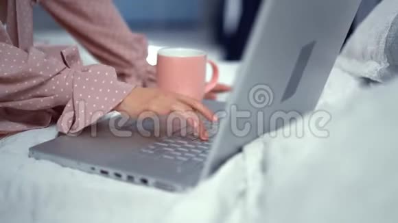 穿着粉色连衣裙坐在床上在笔记本电脑上工作视频的预览图