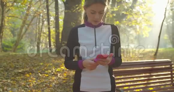 城市公园背景下年轻女性跑步和使用智能手机后的肖像视频的预览图