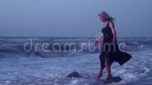 女人努力保持平衡单腿站在石头上在海里跌倒大笑视频的预览图