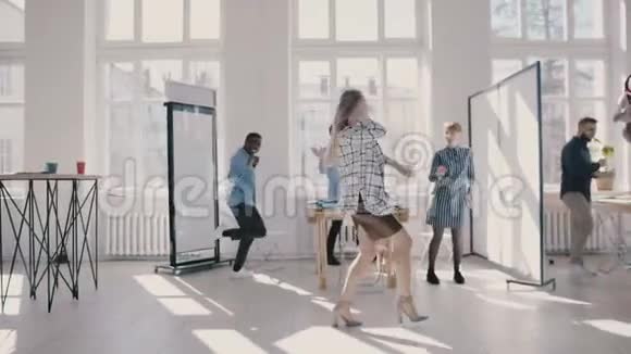 年轻快乐的白人女性老板在现代办公室跳舞与多民族同事一起庆祝慢动作视频的预览图
