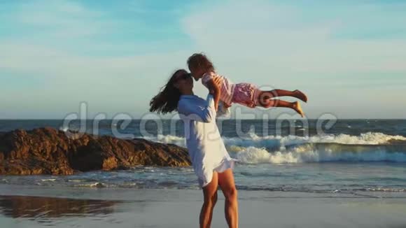 妈妈抱着笑的小女儿在沙滩上旋转视频的预览图