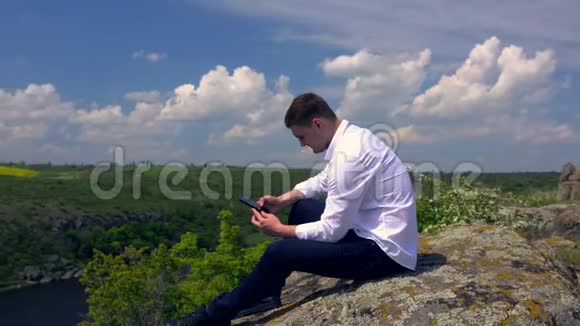 年轻人用手机坐在岩石上视频的预览图