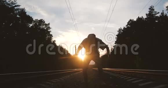 4k一个年轻人在火车轨道附近跳舞的剪影与太阳相对动作缓慢视频的预览图