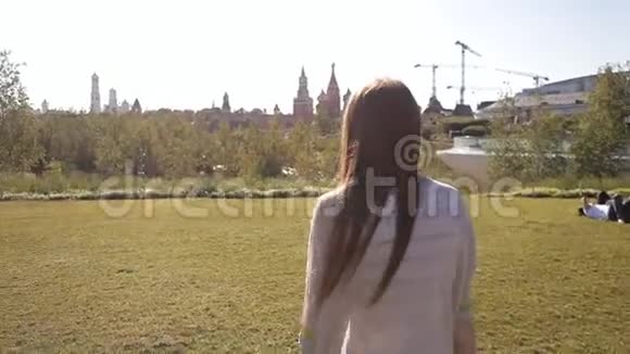 年轻迷人的女人正走在公园里的绿色草坪上微笑着自然与现代建筑视频的预览图
