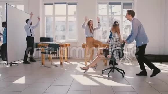 慢动作有趣兴奋的女商人骑着椅子沿着大办公室庆祝在多民族工作场所的晋升视频的预览图
