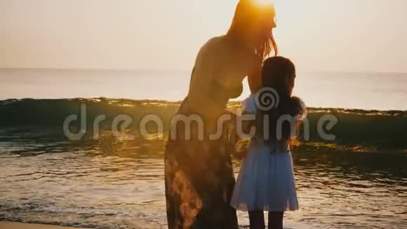 幸福的年轻母亲抱着和纺小女儿微笑着在史诗般的金色日落海滩家庭旅行的概念视频的预览图