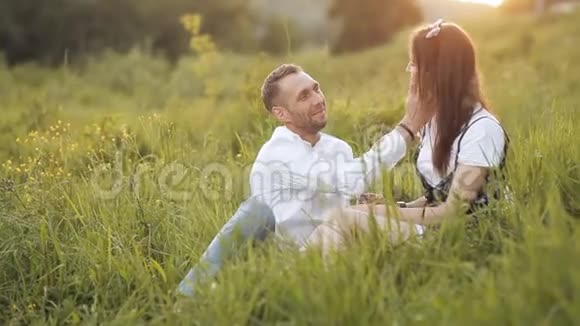 一对年轻夫妇坐在一片明亮的绿色草地上恋爱中的情侣微笑在外面享受温暖的时光视频的预览图