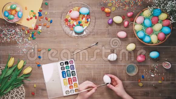 人类手在用复活节彩蛋装饰的桌子上画复活节彩蛋顶部视图视频的预览图
