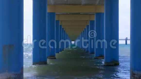 在平行的蓝色柱子之间的码头下的海在水中形成狭窄的走廊视频的预览图