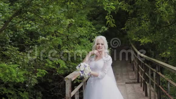 美丽的金发新娘在靠近森林栏杆的桥上视频的预览图
