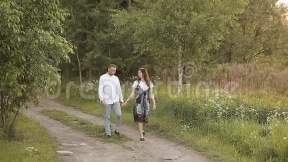 夏天一对年轻的男女牵着手走在公园的一片绿色草地上浪漫爱情关系视频的预览图