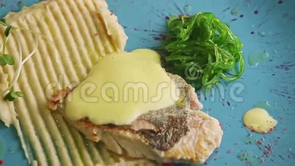 配上酱汁烤鱼土豆泥和海葵在蓝色盘子上旋转视频的预览图