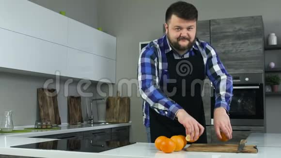 穿着围裙的胖子穿着厨房的傻瓜和一半的橘子一起玩有趣的时刻丰满的男人玩水果视频的预览图