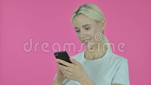 年轻女子在粉色背景下浏览智能手机视频的预览图