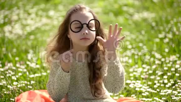戴眼镜的女孩在阳光明媚的日子坐在洋甘菊的田野里户外可爱的小女孩快乐的女孩肖像儿童时尚视频的预览图
