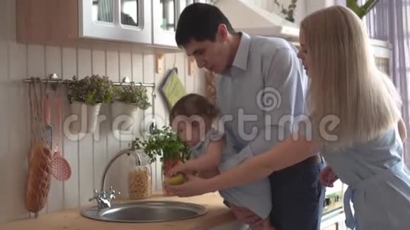 爸爸把女儿抱在怀里带到水槽里女儿抱着一个绿色的苹果妈妈站在附近视频的预览图