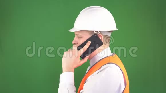 一个穿着白色防护头盔和信号背心的人在一个建筑工地上打电话绿色背景视频的预览图