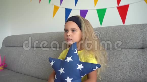 卷发女孩抱着星星形状的枕头坐在沙发上看电视万向节运动视频的预览图
