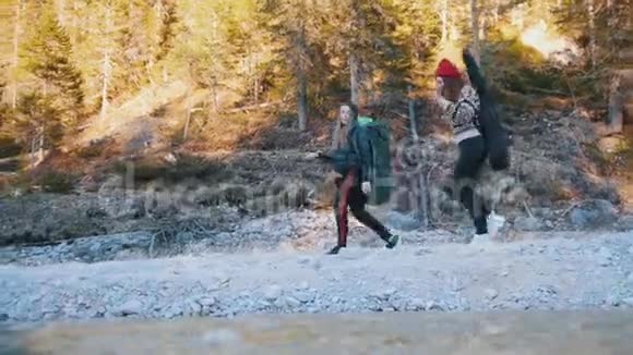 两个年轻的女人在森林和山的背景下背着背包和吉他沿着岩石小径散步视频的预览图
