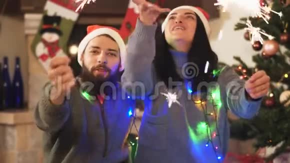 男人和女人坐在圣诞树附近手中挥舞着火花女人送礼物给男人他们接吻视频的预览图