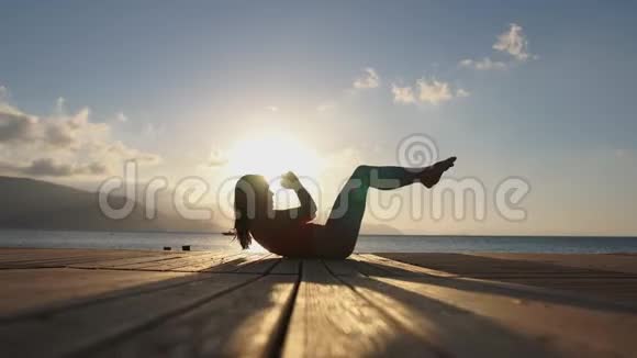 4K一个女人在日出时在海边做腹肌练习动作缓慢视频的预览图