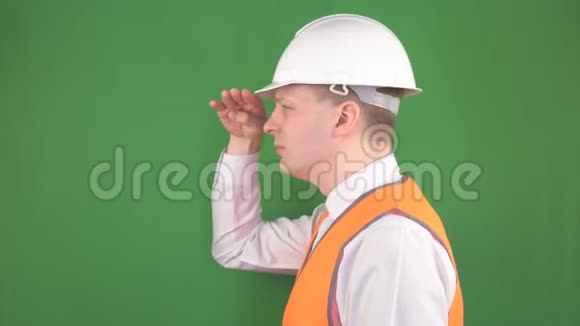 戴着防护头盔和信号背心的男领班在一个建筑工地上看着远处绿色视频的预览图