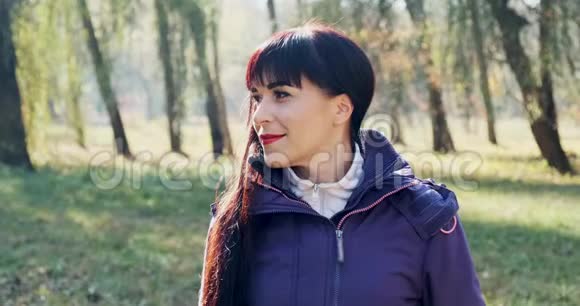 年轻迷人的黑发女人的肖像她微笑着看着秋天公园的相机快乐漂亮的女人视频的预览图