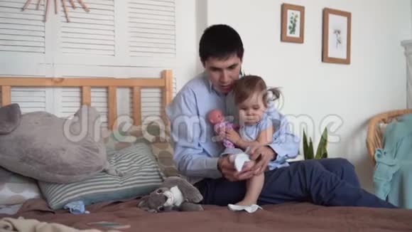 爸爸坐在床上和他的小女儿一起穿上袜子爸爸把女儿抱在怀里视频的预览图