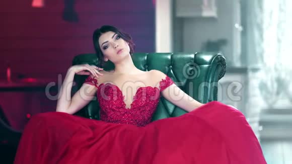 穿着红色晚礼服坐在扶手椅上看镜头的性感时尚女性画像视频的预览图