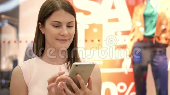 慢动作年轻女子坐在购物中心微笑用她的智能手机和朋友聊天视频的预览图