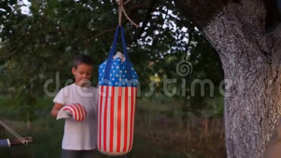 父亲教儿子拳击在房子附近的花园里用带有美国符号的梨进行户外训练父亲视频的预览图