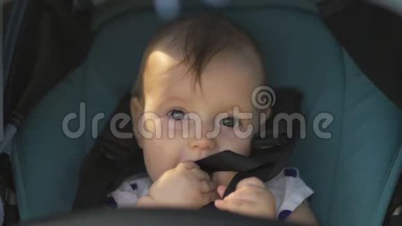 特写可爱的女孩看着坐在蓝色婴儿车里的镜头微笑家庭价值观暖色夏景视频的预览图