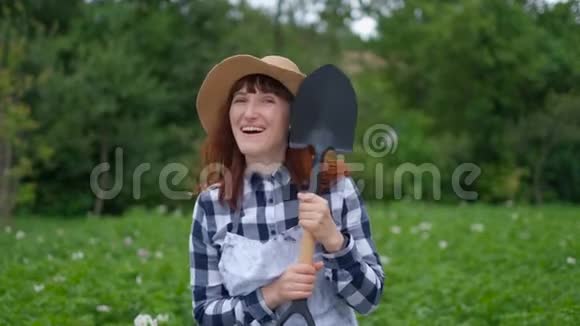 年轻的女农夫拿着铲子在花园里微笑视频的预览图