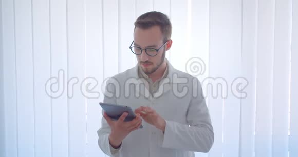 年轻英俊的白种人男医生手持平板电脑在镜头中显示绿色屏幕视频的预览图